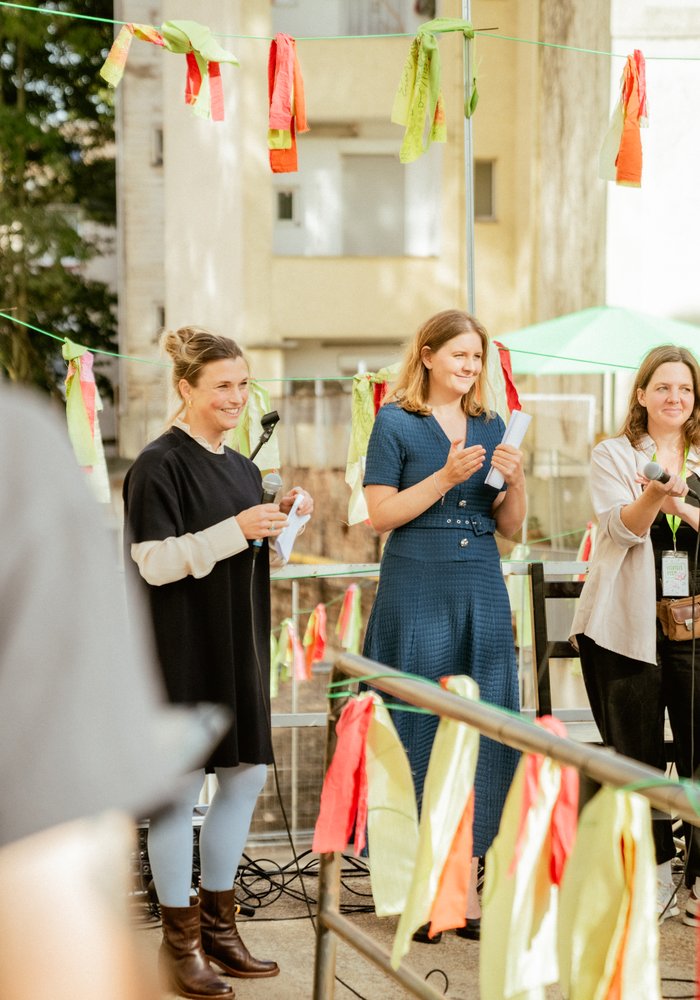 Vier Frauen stehen zusammen auf einer dekorierten Bühne und sprechen in Mikrofone.