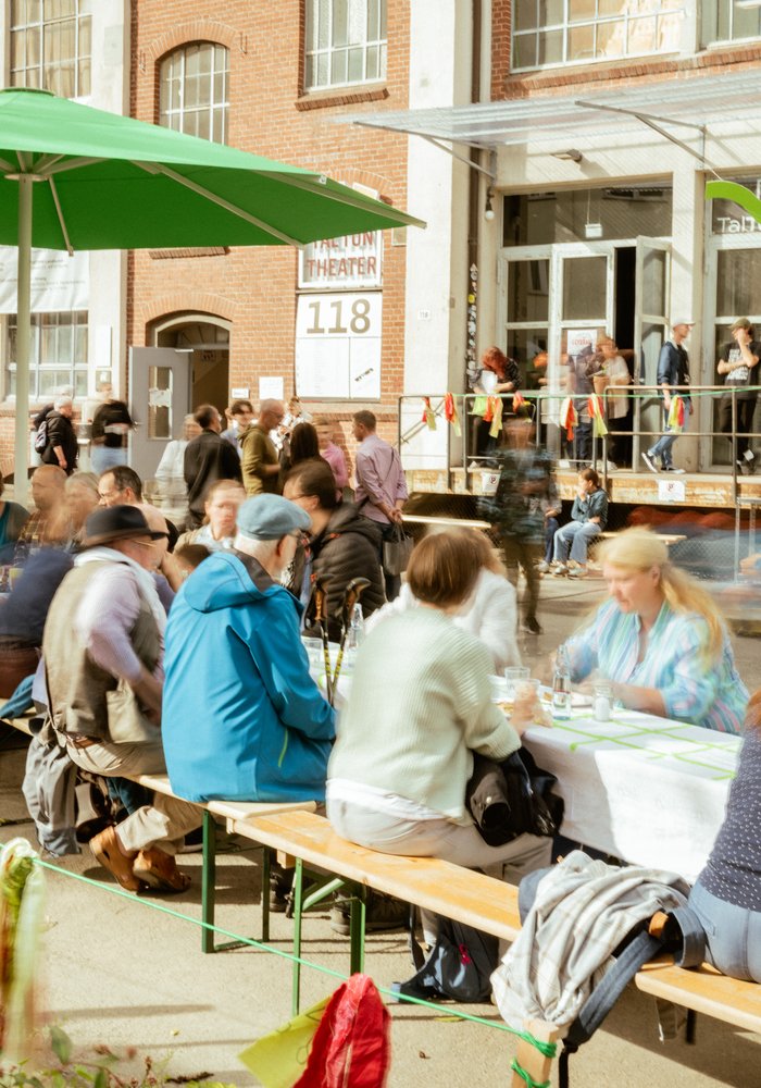 Viele Menschen sitzen an hintereinander aufgestellten Tischen