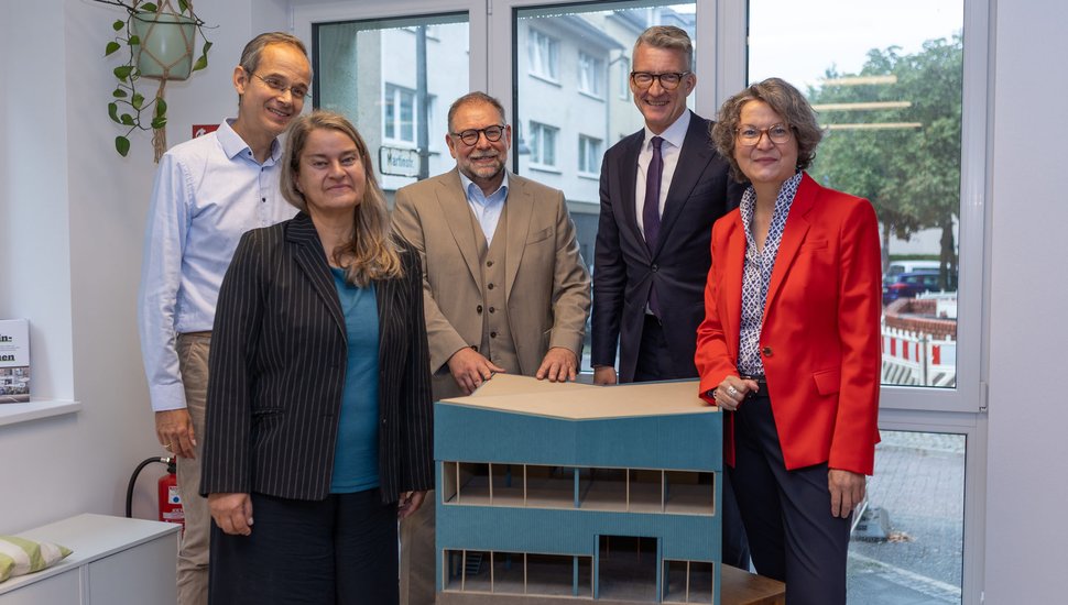 Ina Scharrenbach steht mit Vertreter*innen des HONSWERKs und der Stadt um das Modell der HONSWERKSTATT