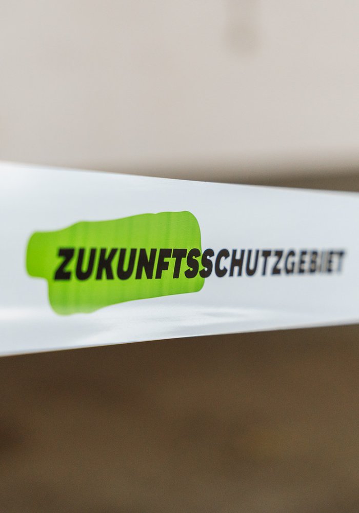 ein Absperrband in weiß, wo "Zukunftsschutzgebiet" drauf steht, mit grünen Akzenten hinterlegt
