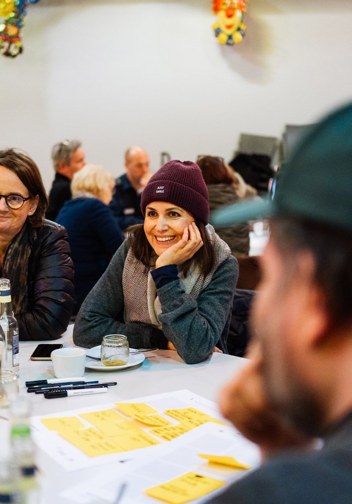 Teilnehmer*innen des Workshops sitzen um einen Tisch und diskutieren, wobei Annette Bederke und noch eine Teilnehmerin im Fokus sind.
